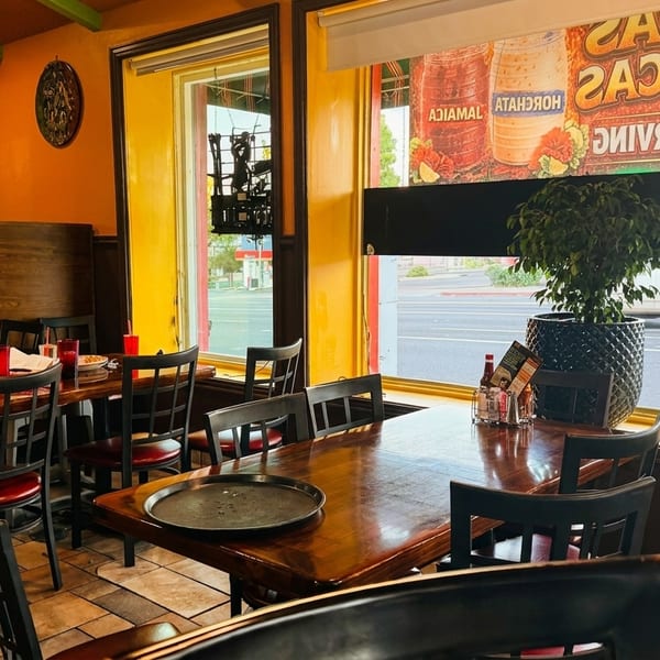 Restaurant interior with wooden tables, red chairs, and a large window looking out onto a street.
