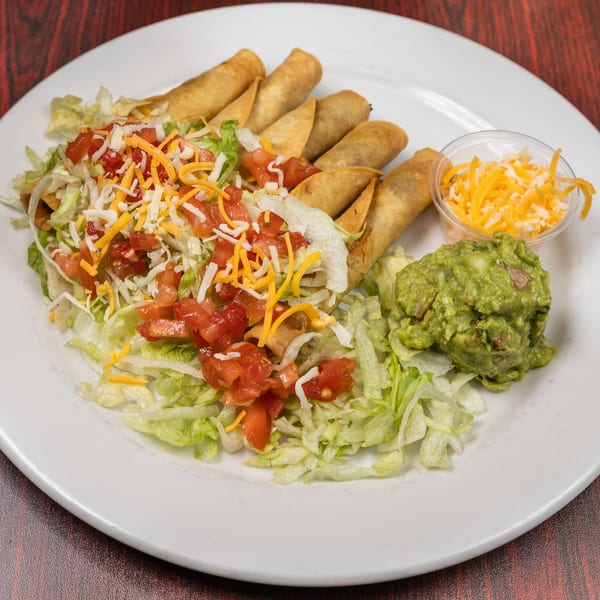 Crispy taquitos with shredded lettuce, diced tomatoes, cheese, guacamole, and extra cheese on a white plate.