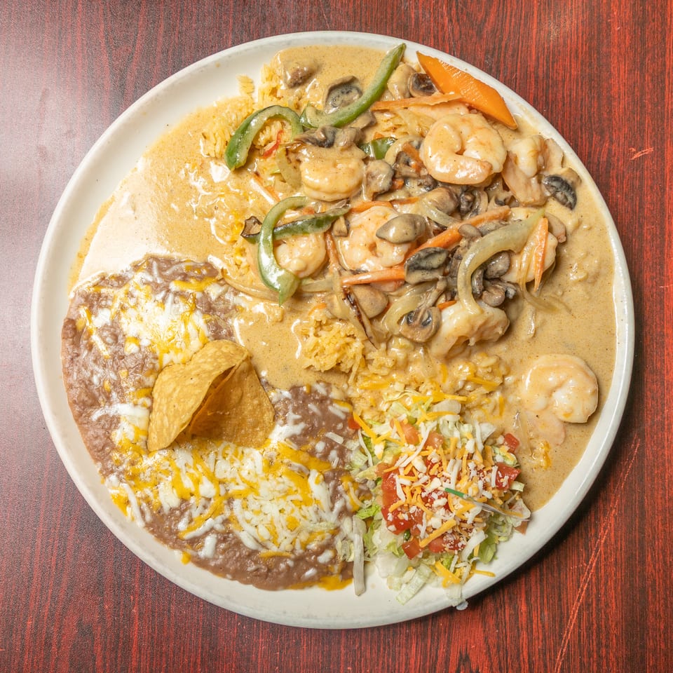 Plate of shrimp with vegetables in cream sauce, refried beans, rice, and a side salad.