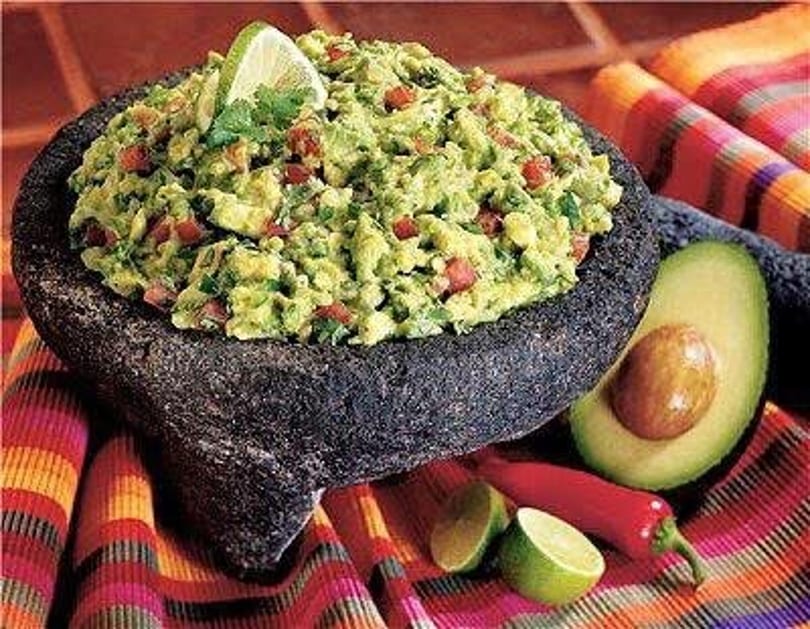 Fresh guacamole in a stone molcajete, garnished with lime, cilantro, avocado, and chili peppers.