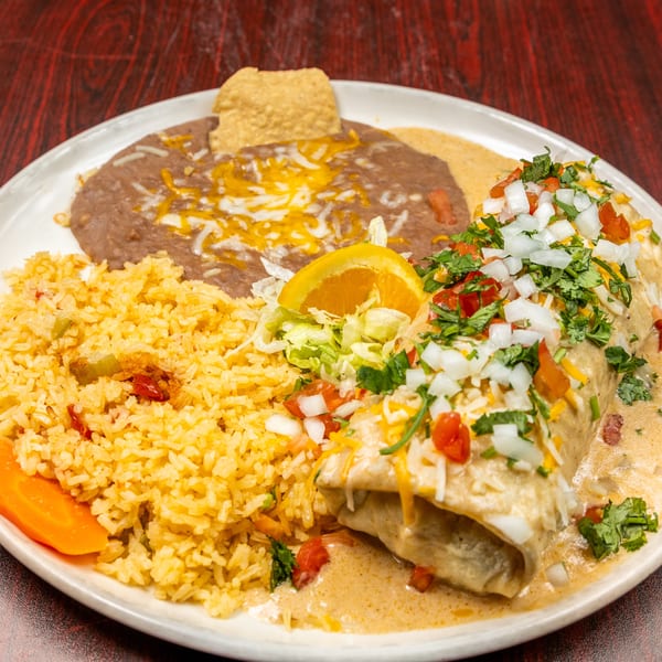 Burrito covered in sauce, cheese, and pico de gallo, served with rice, refried beans, and an orange slice.