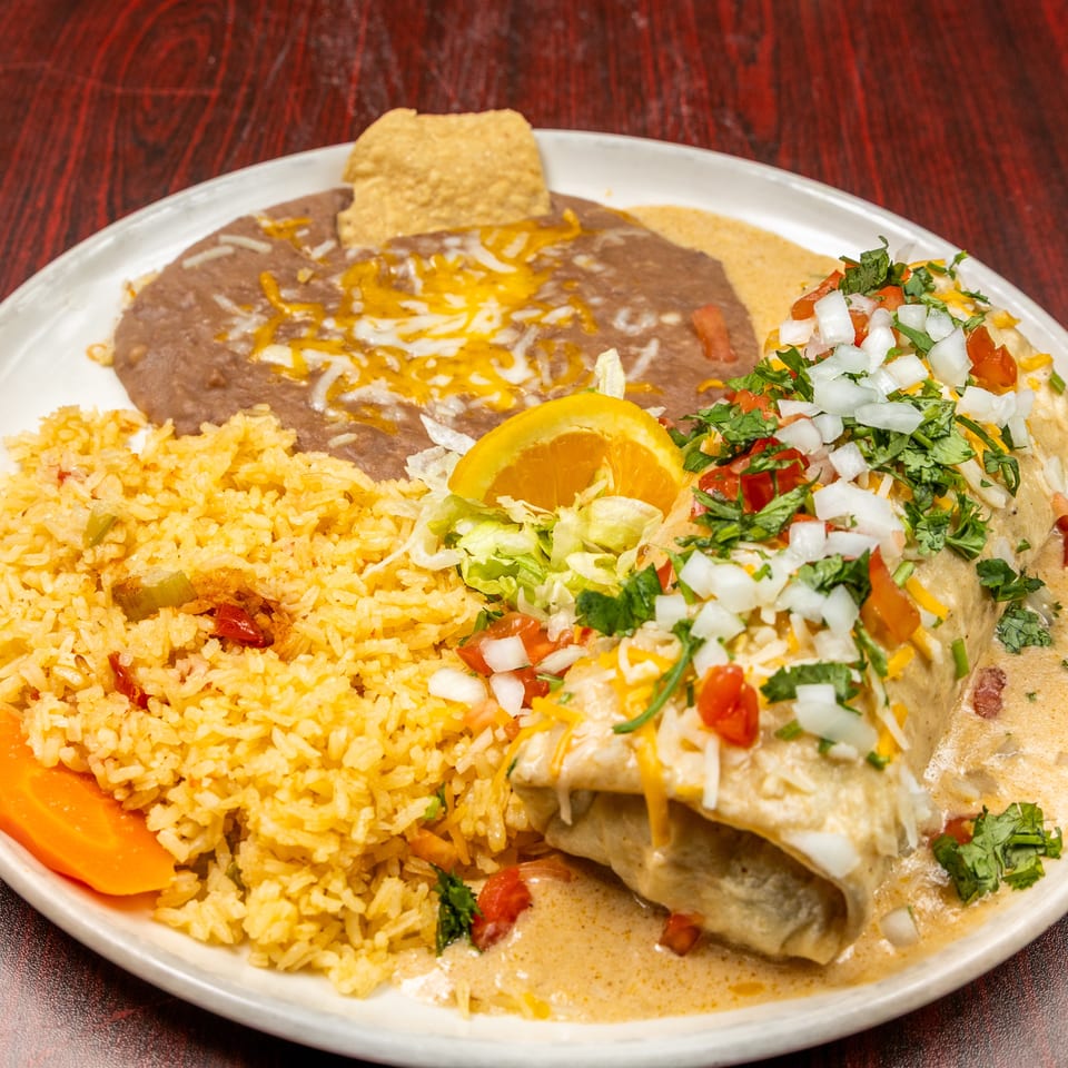 Burrito covered in sauce, cheese, and pico de gallo, served with rice, refried beans, and an orange slice.