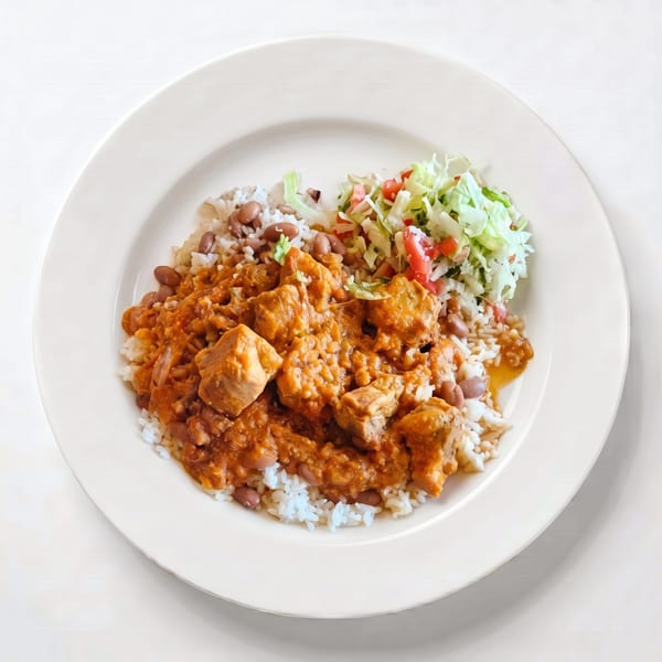 A plate of chicken curry with rice, beans, and a side salad on a white background.