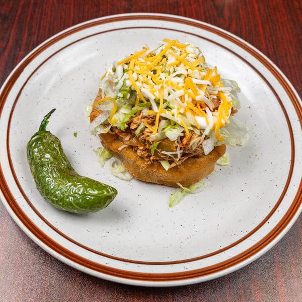 Fried tostada topped with shredded meat, lettuce, cheese, and a roasted green pepper.