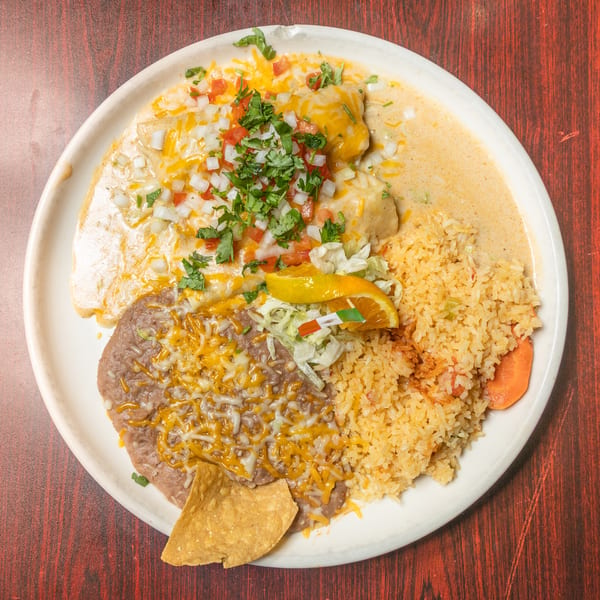 Cheesy enchiladas topped with pico de gallo, refried beans, rice, and a tortilla chip on a white plate.