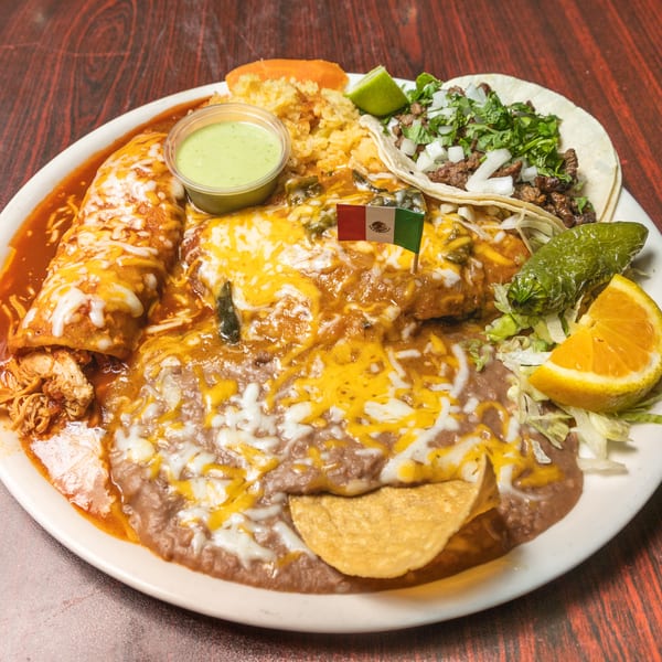 Mexican platter featuring enchiladas, a taco, rice, refried beans, and a small Mexican flag.