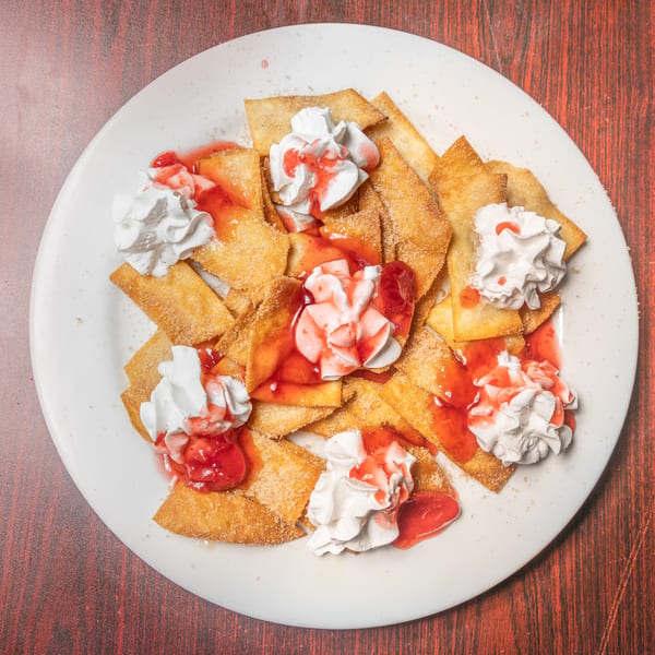 Golden fried dessert chips topped with whipped cream and strawberry sauce.