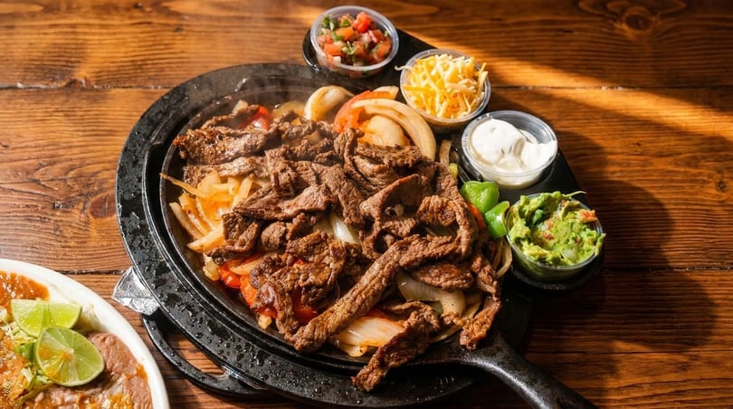 Sizzling steak fajitas with onions and peppers, served with sides of guacamole, sour cream, and salsa.