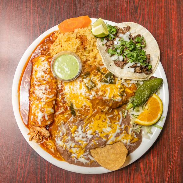 Mexican combo plate with a cheesy enchilada, steak taco, rice, refried beans, and fresh garnishes.